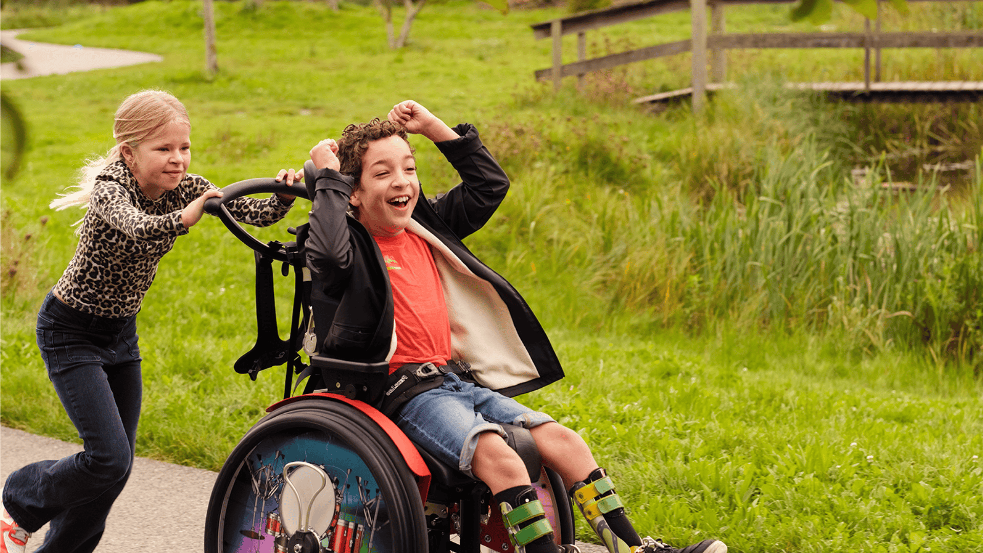 Kind in een rolstoel is heel blij. Hij wordt geduwd door een meisje